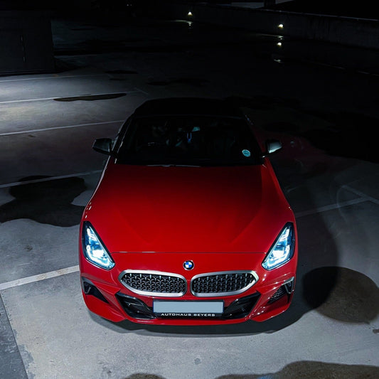 Red BMW car parked in a dark parking lot with illuminated headlights.