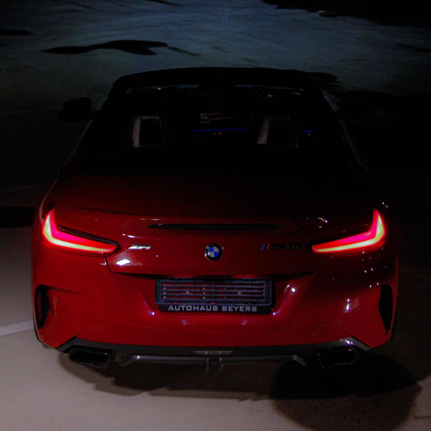 Red BMW car with illuminated taillights on a dark street.