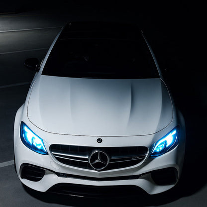 Front view of a white Mercedes-Benz car with illuminated headlights on a dark background