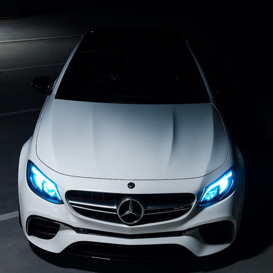 Front view of a white Mercedes-Benz car with illuminated headlights on a dark background
